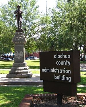 A Confederate statue stands behind a county public building sign.