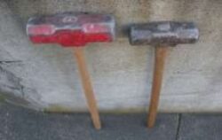 Two sledgehammers stand against a wall, one red and one metal gray.