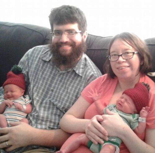 A couple smiles at the camera; each person holds a baby.