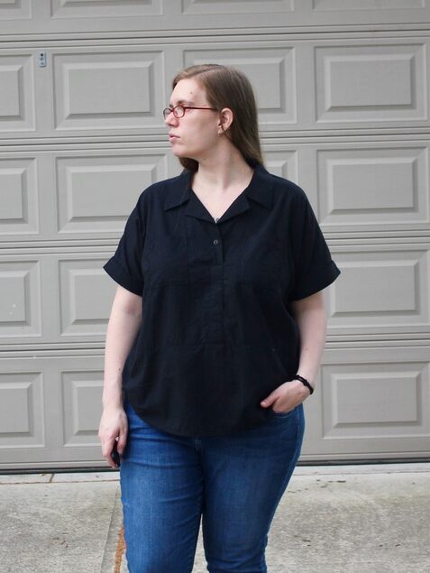 A woman with long hair looks off to one side; she wears  black shirt and jeans.