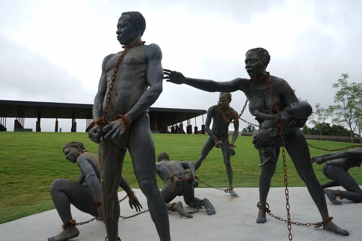 A sculpture featuring six enslaved persons in chains. In the foreground a woman holding a child reaches for a man. Behind them, three of the figures are kneeling and one looks on in horror.